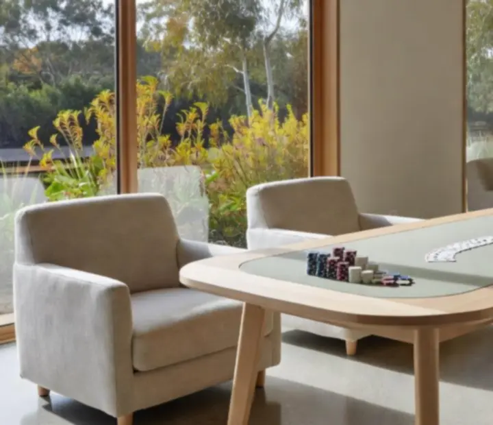 Custom pale timber poker table and low-slung armchairs in a bright lounge